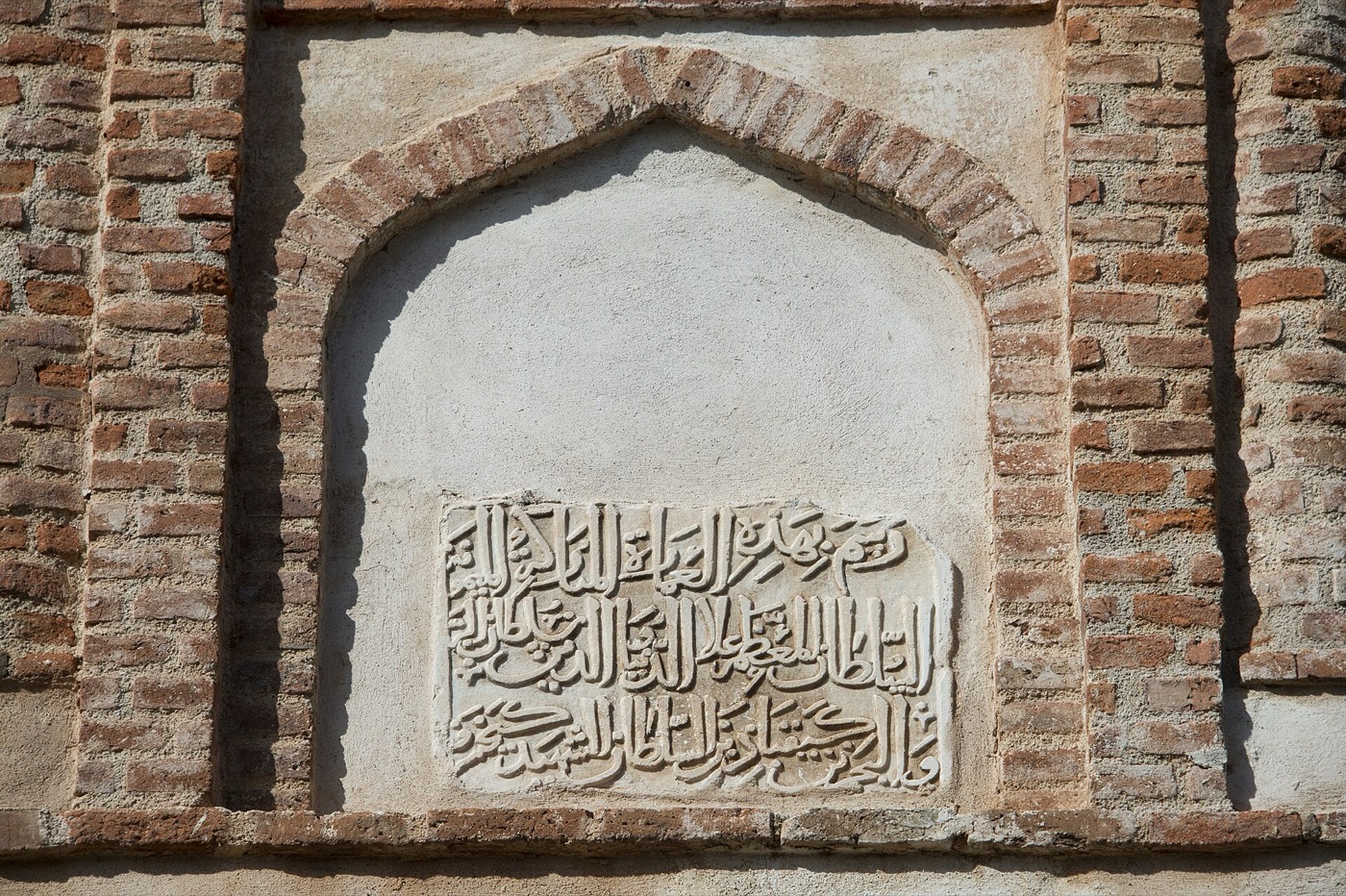 Close-up of an arched brick wall with Arabic calligraphy carved in stone